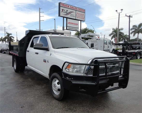 White Ram 3500 SLT dump truck with black grille guard and dump bed in a dealership lot. Signage in background reading TLC Truck Sales Center and Jordan dealership.