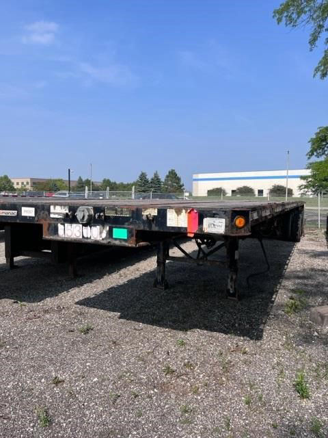 Flatbed trailer showing rear and deck surface with multiple reflective plates and lights.