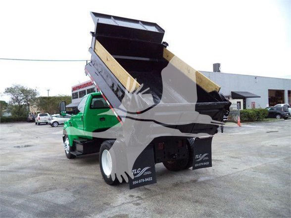 Dump truck with a green cab and black dump bed raised in a dealership lot. Visible text on the wheels and body includes TLC and phone numbers.