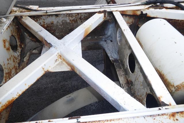 Structural frame of a Fruehauf dry bulk trailer showing rusted white-painted cross members and a large cylindrical tank side with holes.