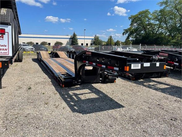 Lowboy trailer with 24ft steel roller paver deck, black frame, stock trailer yard, Fontaine 55-ton equipment in background.