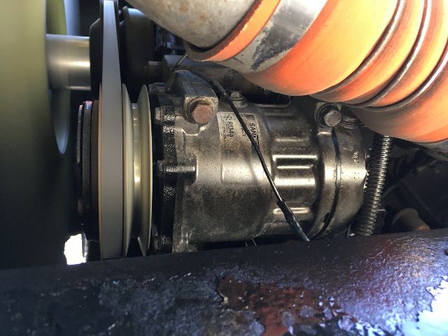 Close-up of a Kalmar Ottawa YT30 yard truck engine bay showing a belt-driven component with a pulley and an orange-orange cushioned hose nearby.