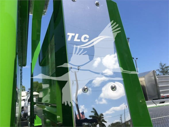 Peterbilt 337 truck component with TLC branding on chrome panel and green frame, clear sky reflected.