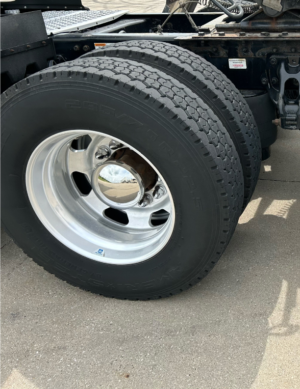 Twin Kenworth truck rear wheels with polished chrome hubs and heavy-duty tires in a truck yard.