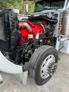 Peterbilt engine bay with red engine block and front wheel visible, cooling system components, and belts.