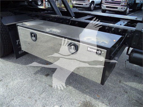 Peterbilt 367 truck bed toolbox mounted under chassis showing metal storage box with two latches and a lock; chrome badge on right side.
