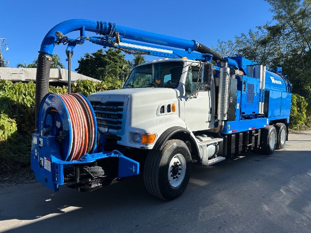 Sterling L7500 vacuum truck with a blue hose reel on the front, white cab, and blue body equipment. Side view showing long vacuum unit and elevated boom.