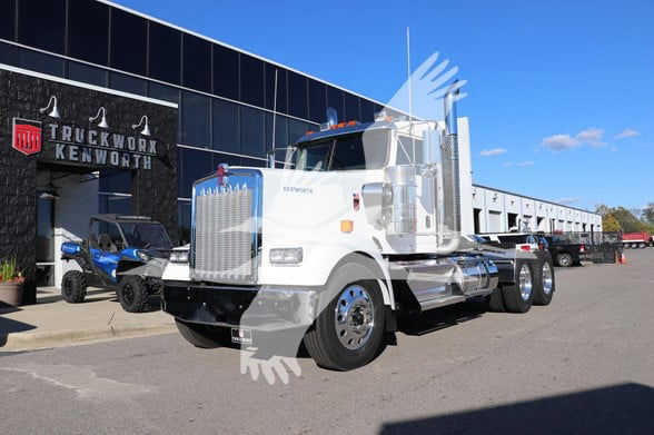 Kenworth W900L heavy duty truck in dealership lot with chrome exhaust stacks and large vertical grille.