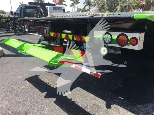 Peterbilt 337 flatbed rear with green loading ramps and tail lights visible; no identifying stickers legible other than generic vehicle and trailer components.