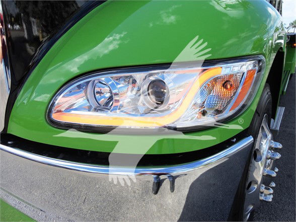 Front left headlight of a green 2022 Peterbilt 337 truck. Visible details include the headlight assembly with clear lens, amber turn signal, chrome bumper, and wheel with dual tires.