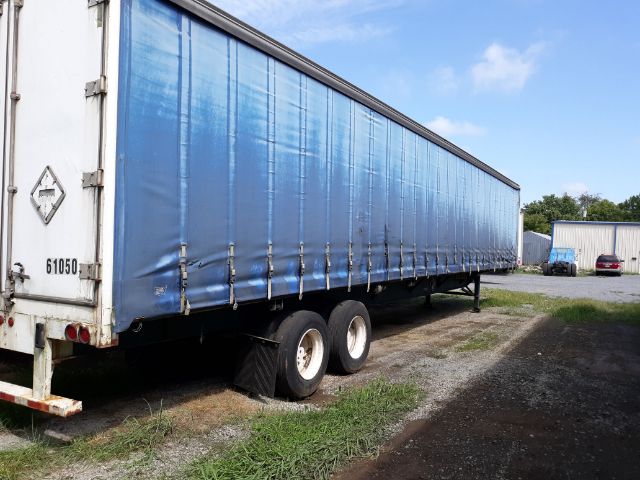 Trailer side view showing blue curtain with rear doors labeled 61050 and a two-axle wheel setup. There is a white rear frame with diamond-shaped placard and a small portion of a ramp.