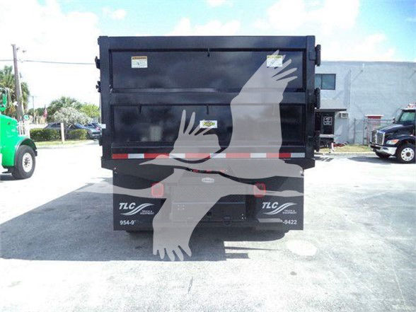Rear view of a 2016 Hino 268A dump truck with a black dump bed and TLC logos; empty lot with other trucks in the background.