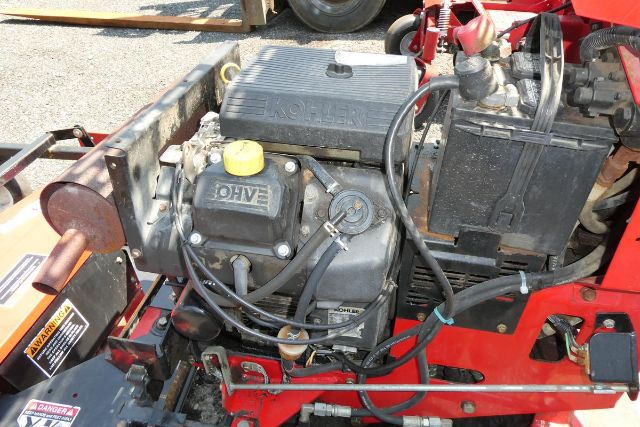 Kohler engine bay showing gasoline-powered Kohler engine with yellow oil cap and surrounding hoses and battery in red frame.