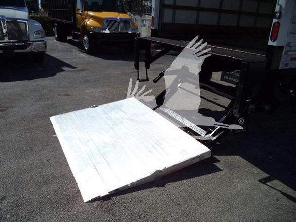 Truck flatbed ramp or lift platform attached to a box truck, white wooden surface with metal frame and hydraulic mechanism visible.