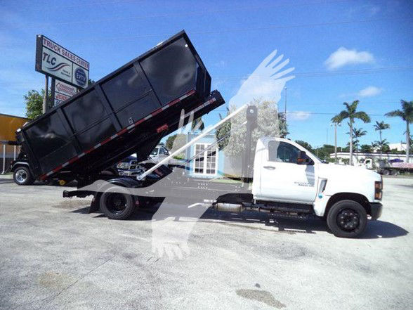 Truck in a lot with a raised black dump bed on a white Chevrolet Silverado 6500HD cab; clear blue sky.