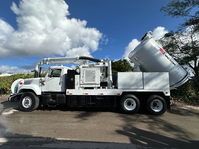 Wheel-right side view of a white International vacuum truck with a mounted large cylindrical tank and hoses, on a sunny day.