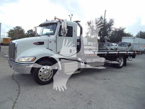 Truck cab and flatbed trailer, Peterbilt 337 style, light gray/white color. Large front grille, dual-axle rear, with service decals and windows. Overlay watermark with hands on image.