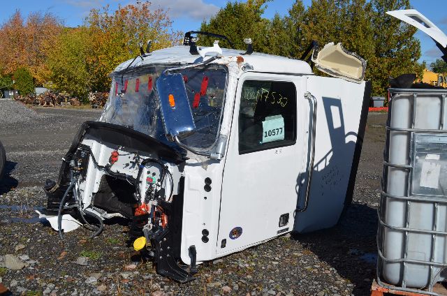 Cabover truck cabin front end with damaged windshield and exposed dashboard components, white exterior, truck label visible on the side window.