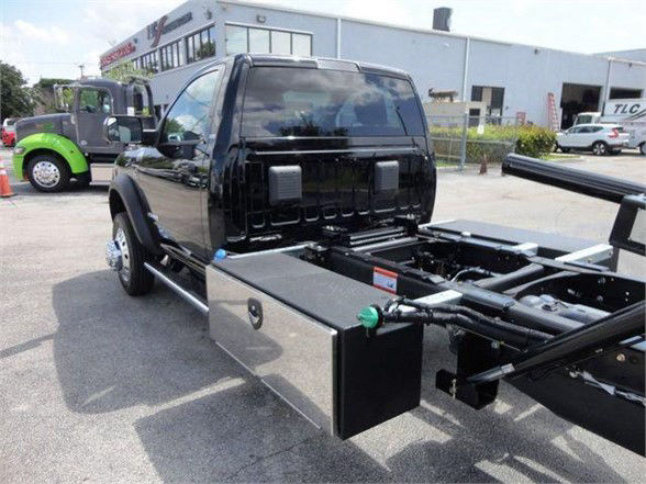 Vehicle chassis with a metal toolbox and tow hitch on a Ram 5500 cab; flatbed frame visible with hydraulic components and storage box.