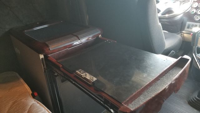 Conventional sleeper truck cab interior showing a black center console/armrest with a mounted toolbox lid and side panels.
