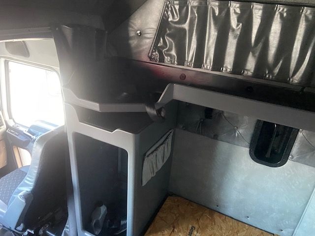 Interior sleeper cab area of a 2015 Mack CXU613 showing bunk storage shelves and partition, grey panels, and a window to the left.