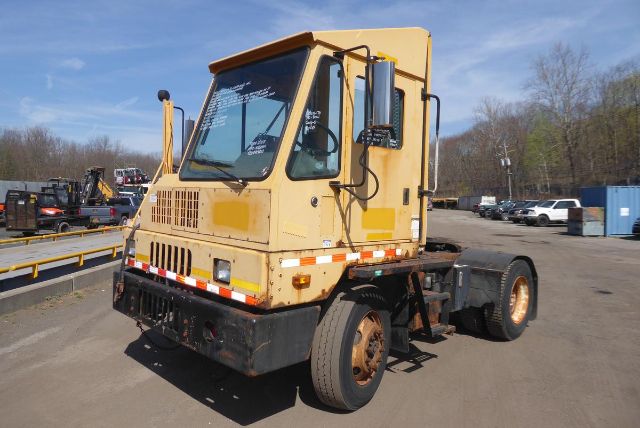 Kalmar yard truck in yellow, side view showing cab with large windshield, rear chassis, and single rear axle; orange accents and black bumper; some wear.