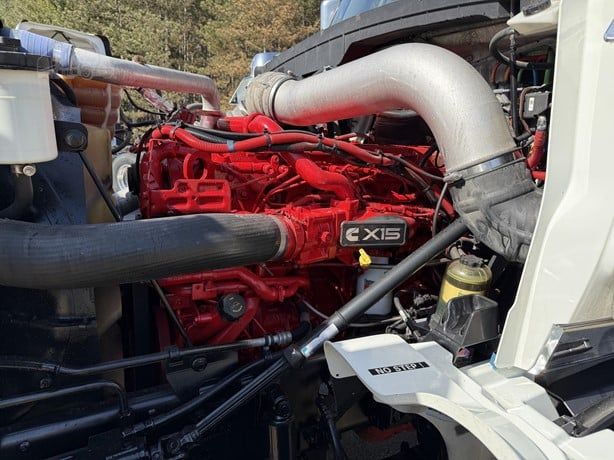International Lonestar truck engine bay showing red X15 engine with intake manifold, large silver exhaust pipe, black coolant hose, and various hoses and components.