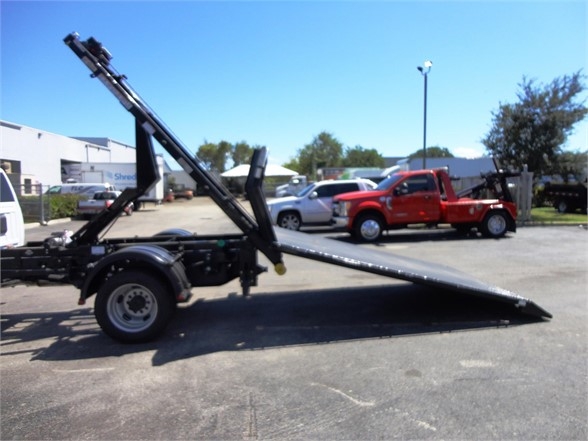2024 Ram 5500 HD hooklift truck in a parking lot showing a raised hoist and hydraulic arm with a long ramp.