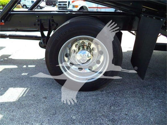 Wheel and tire on a truck chassis with a chrome hubcap, view of the trailer axle and suspension components under a Ford/International-style truck frame.