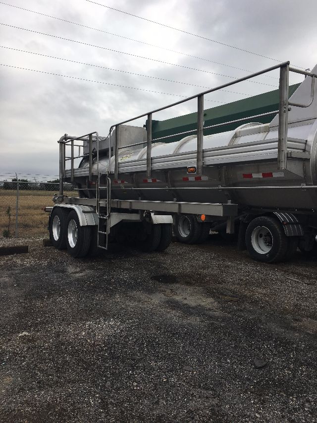 Trailered tanker trailer in-service with dual rear axles and metal railing, side view showing cylindrical tank and ladders.