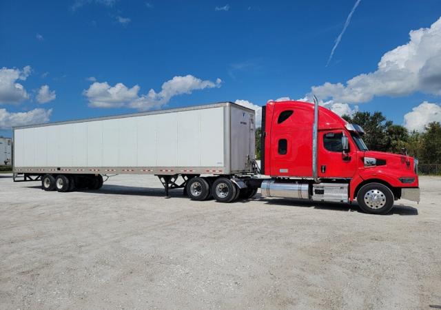 Western Star 4900 conventional sleeper truck with a red cab and a long white trailer, parked on a gravel lot under blue sky.