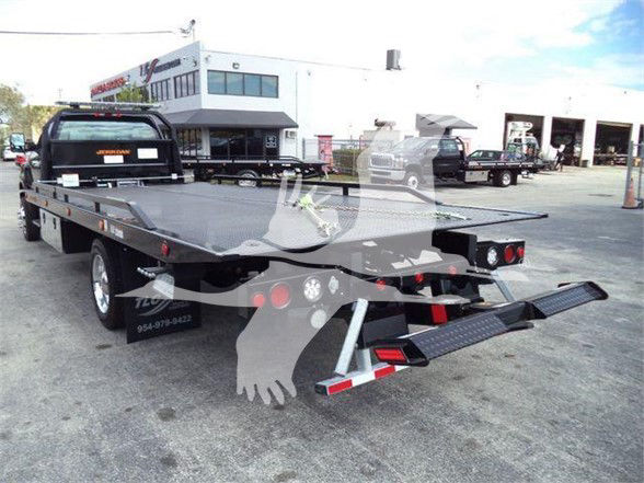 2023 International CV tow truck flatbed with rear loading ramps and black bed, service yard with buildings in background.