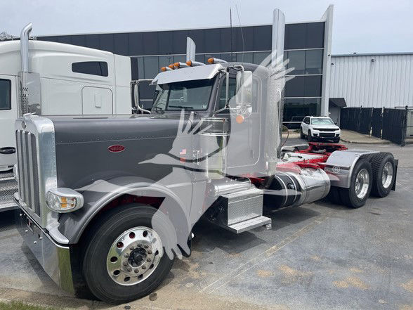 Peterbilt 389 conventional daycab truck in a lot, chrome exhaust stacks, sleeperless, dual rear axles, empty fifth wheel, front view showing grille and headlights.