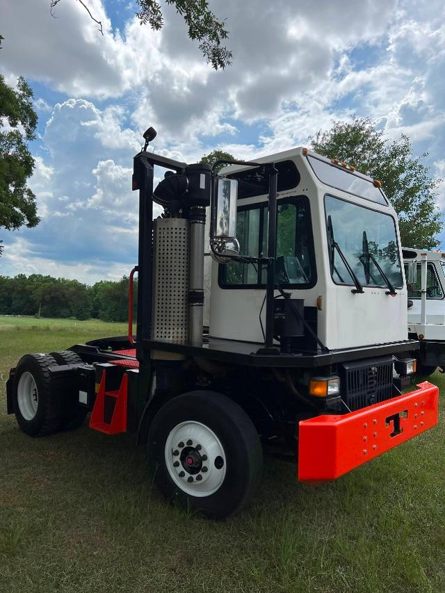 Truck cab of a 2012 Tico Prospotter with black chassis, white cab, and bright orange front bumper parked on grass.