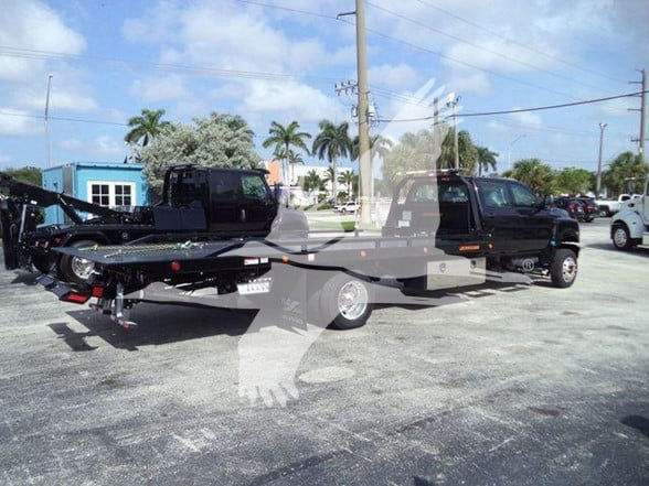 Tow truck with flatbed trailer attached, International CV series, black trucks in background, dealership lot.