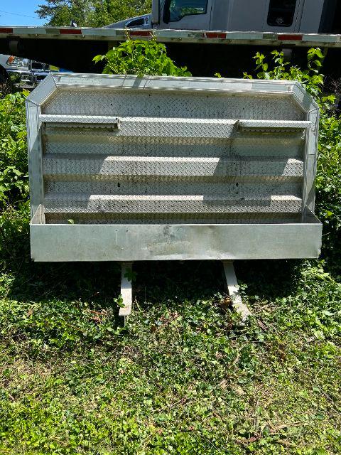 Aluminum headache rack with diamond plate pattern mounted on a truck bed, showing two support legs at the bottom and a ribbed back with shelves.