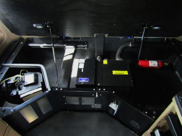 Kenworth truck interior with engine bay and control unit, showing a black box with labels, a red fire extinguisher, and wiring harnesses.
