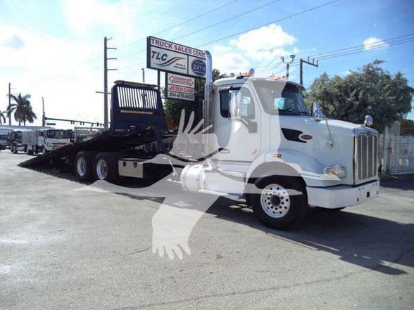 2016 Peterbilt 567 tow truck in a parking lot, front-right view showing a white cab and black flatbed; Stock number sign in background.