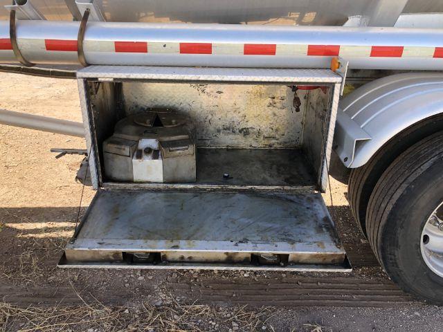 Tank trailer side compartment with open storage hatch showing a plastic jerry can and metal interior.