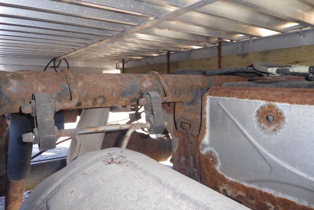 Truck frame with rusty rail and mounting hardware showing a corroded chassis rail and rear suspension components in a storage area.