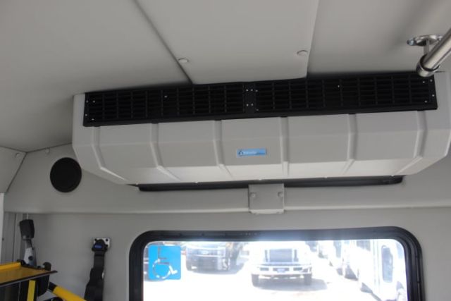 Interior view of a 2025 Ford E450 shuttle bus cabin showing overhead HVAC unit and dashboard window with exterior vehicles visible.