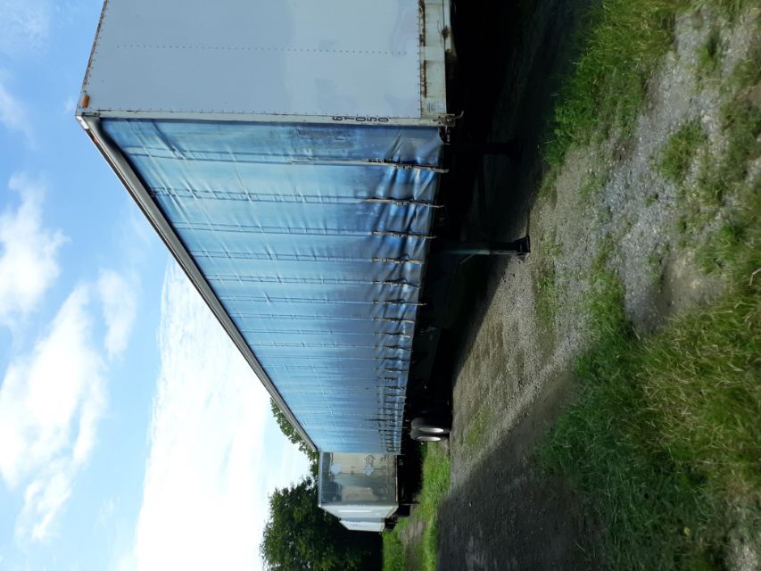 Trailer with blue curtain side and white front, parked on gravel lot, dual rear axles visible.