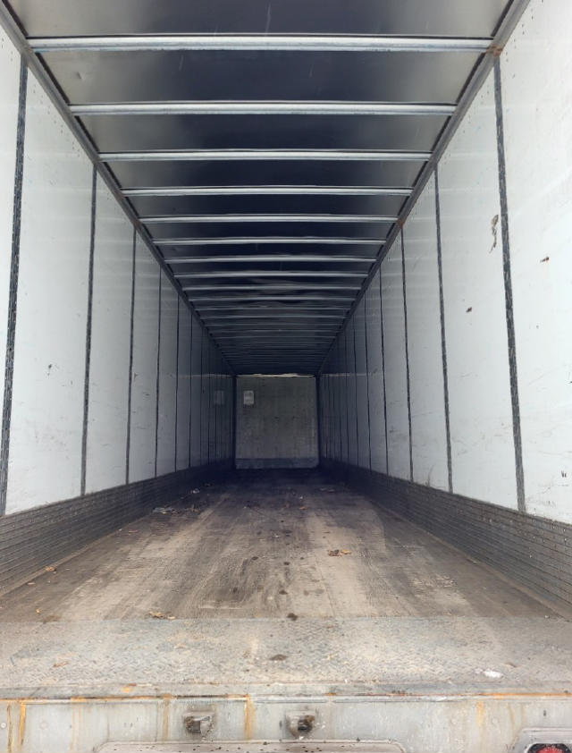 Trailer interior showing empty cargo area with vertical side panels and ribbed ceiling, from rear open doorway.
