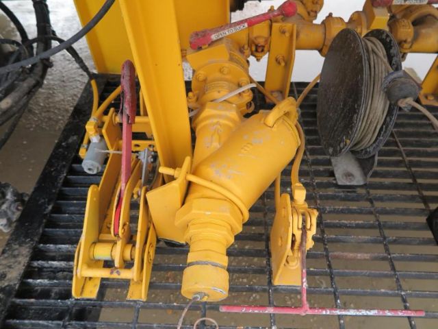 Heavy yellow fuel system component with pump and hoses, tractor-like engine bay view showing piping and mechanical fittings.