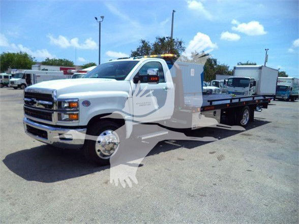 Chevrolet Silverado 6500HD tow truck with a flatbed on a sunny lot. Visible text includes 'CHEVROLET' on the grille and the escorting service markings/logo on the door and side panels.