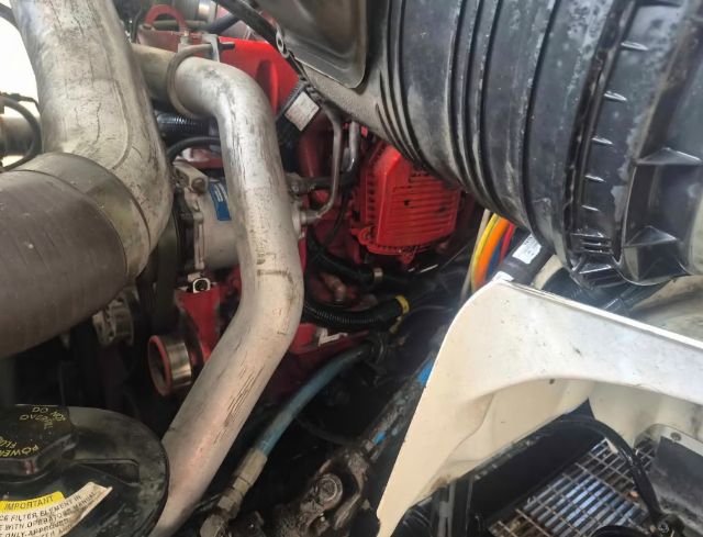Truck engine bay showing large intake tubing, radiator hose, and red engine block with visible hoses and wiring.