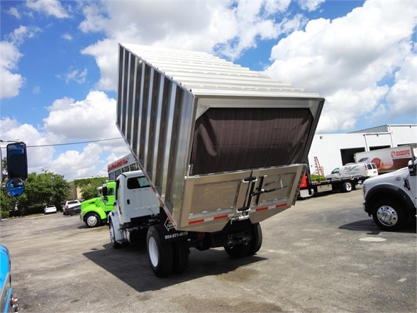 Freightliner Business Class M2 106 rear dump truck bed tilted up in a lot, multiple trucks visible.