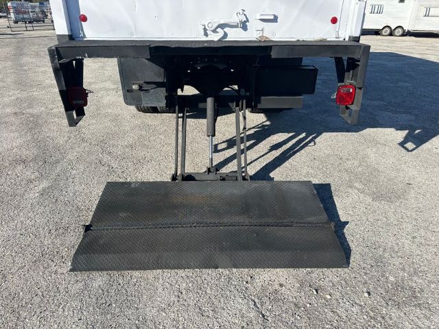 Back view of a 1997 International 4700 box truck showing a deployed ground-level loading ramp, rear bumper, and hydraulic/steering components beneath the cargo area.