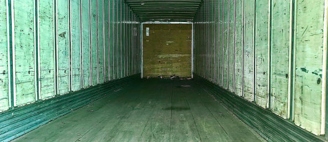 Trailer interior showing empty cargo space with wooden end wall and metal side rails in a green-tinted interior.