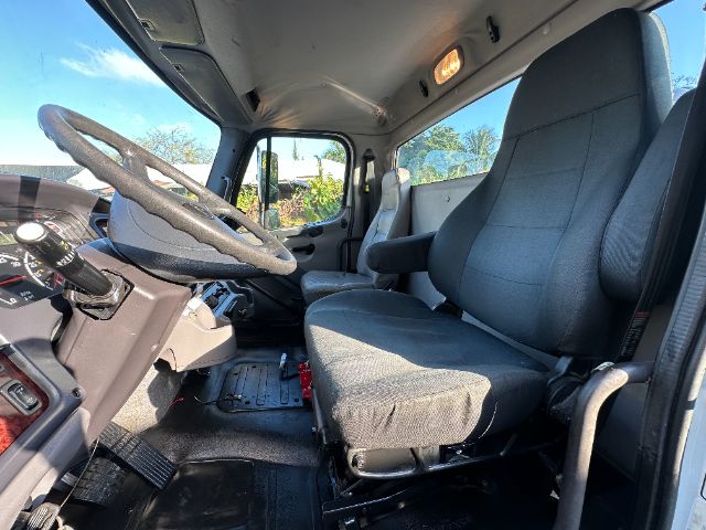 Truck cab interior of a 2014 Freightliner M2 showing steering wheel, driver seat, and dashboard with controls.